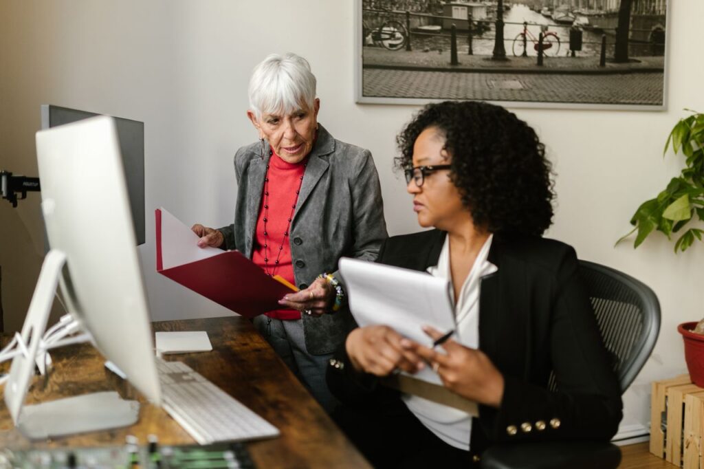 Mastering the First Impression: Your intriguing post title goes here Senior and young women collaborating in modern office setting, discussing documents.